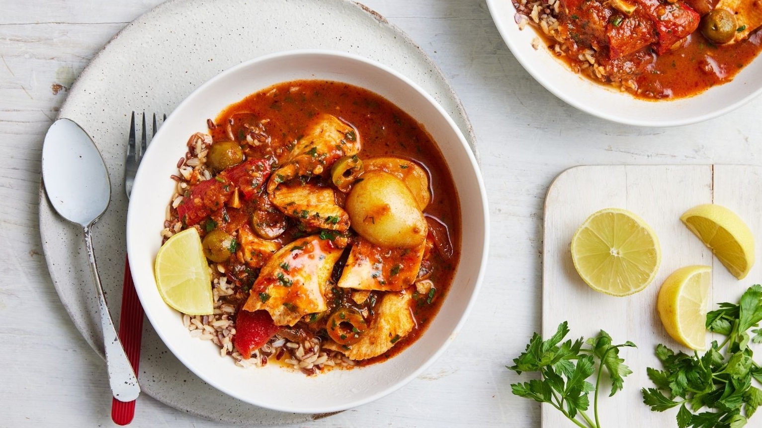 Spanish fish stew in bowls on a white table, with lemon wedges to serve