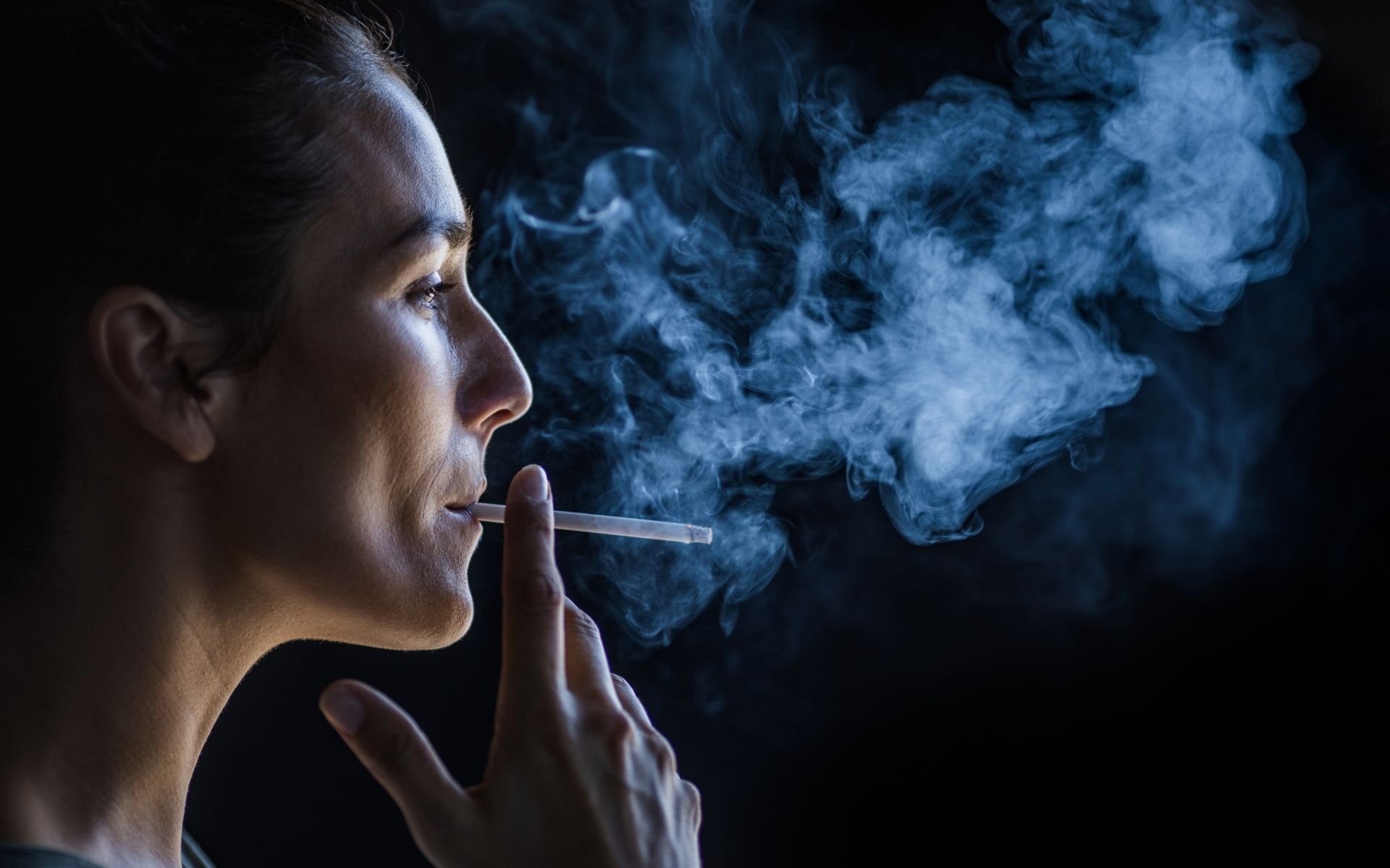 Woman smoking a cigrette with billow of smoke against dark background