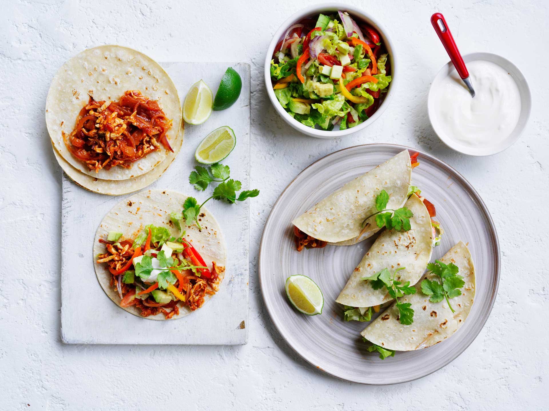 Mexican shredded tofu tacos filled with spiced tofu, salad, avocado, yoghurt and fresh coriander, served with lime wedges.