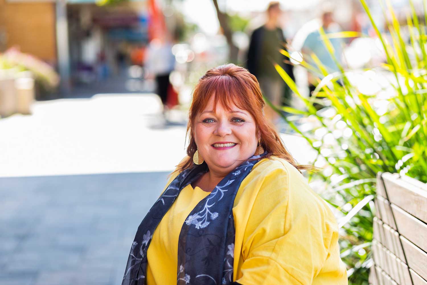 Smiling woman with yellow jacket, blue scarf and bright orange red hair