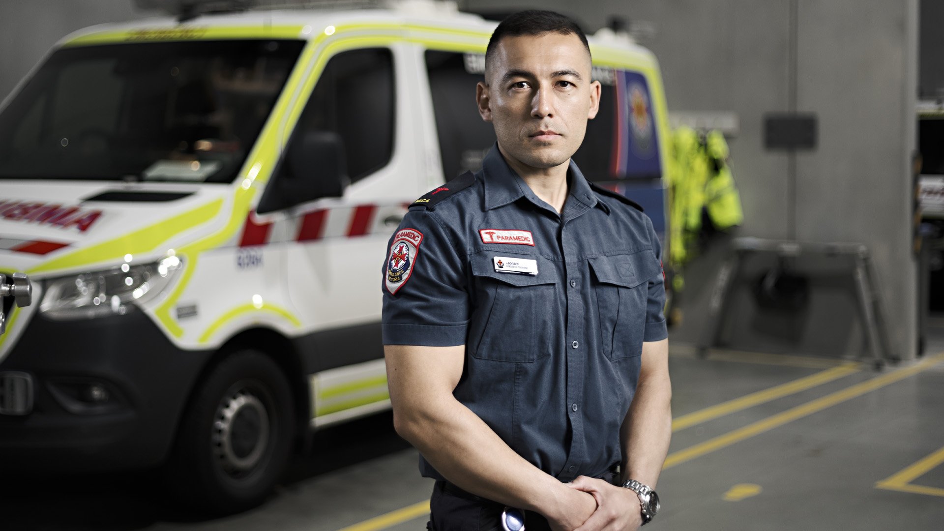 A male paramedic in uniform standing in front of an ambulance
