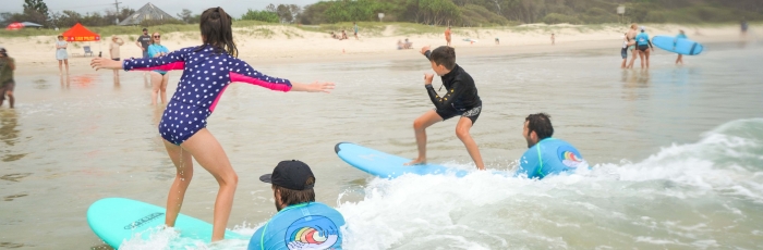 Two kids surfing on a beach being assisted by surfing coaches