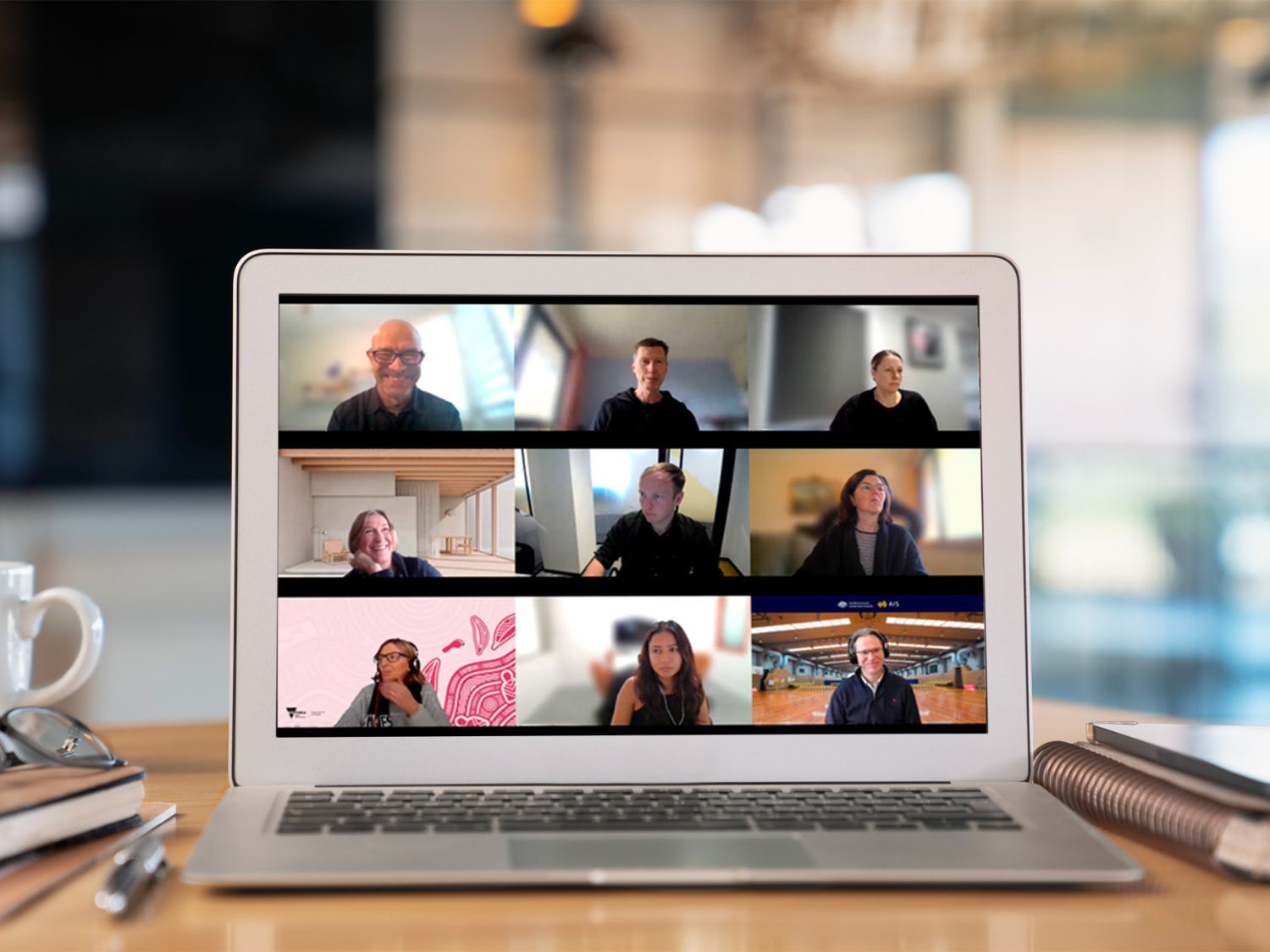 Team video call displayed on a laptop screen, showing multiple people in a virtual meeting at a desk