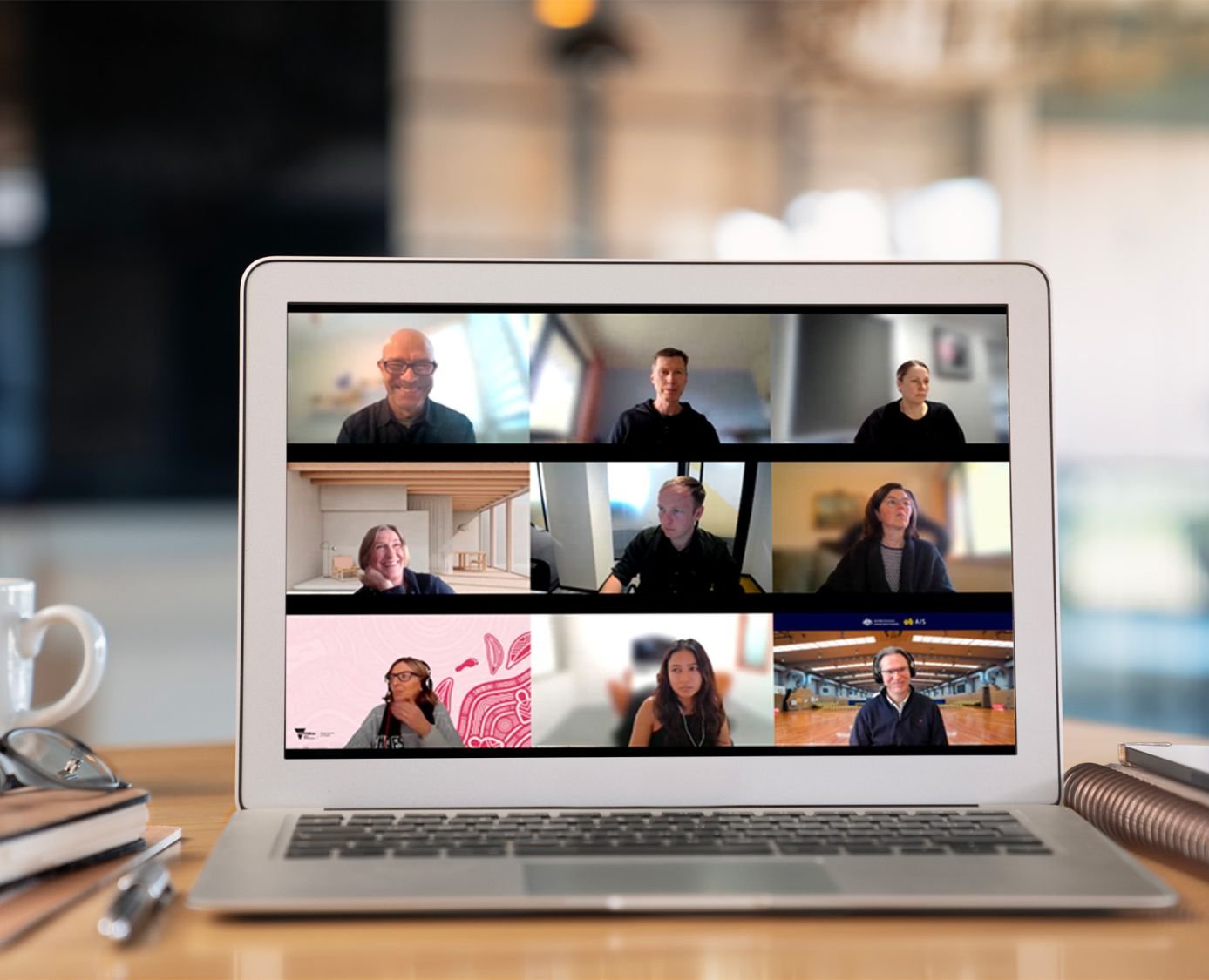 Team video call displayed on a laptop screen, showing multiple people in a virtual meeting at a desk.