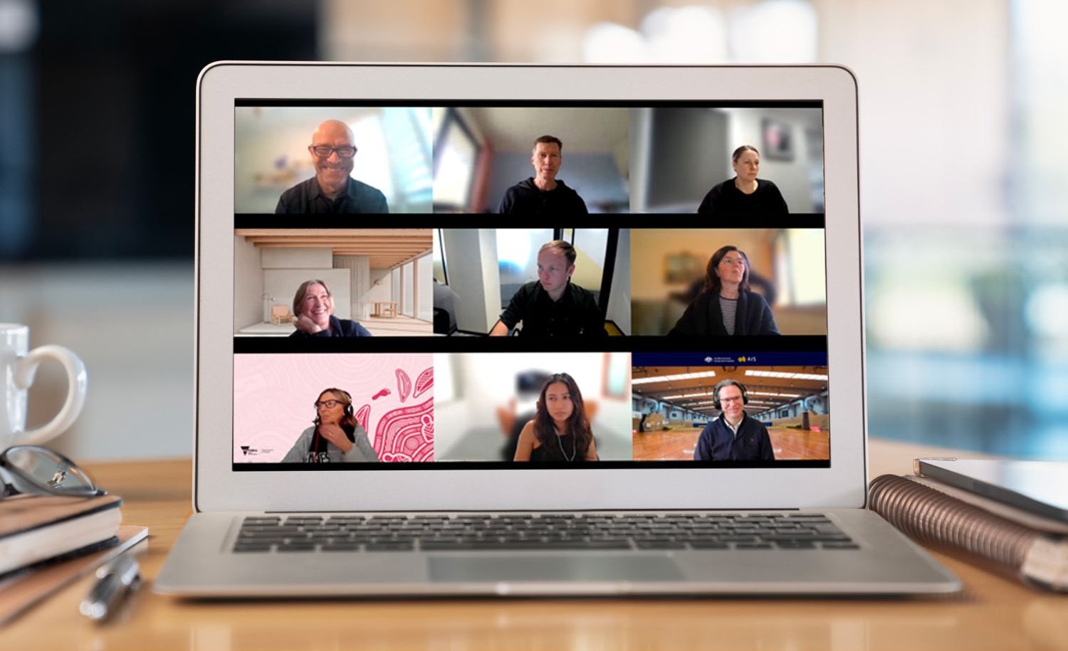 Team video call displayed on a laptop screen, showing multiple people in a virtual meeting at a desk.