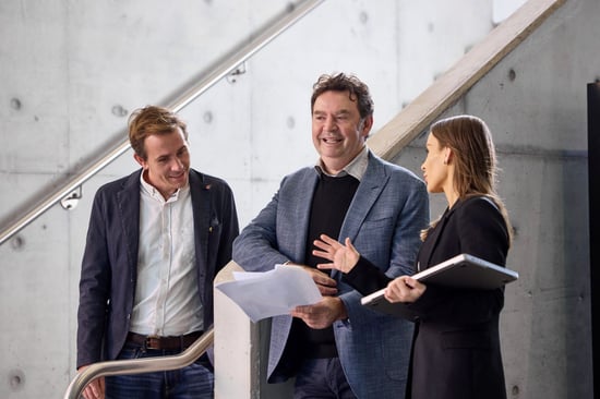 Three people talking together while holding documents and a laptop