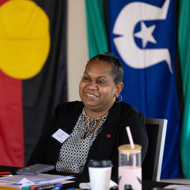 First Nations woman sitting in front of Aboriginal and Torres Strait Islander flags