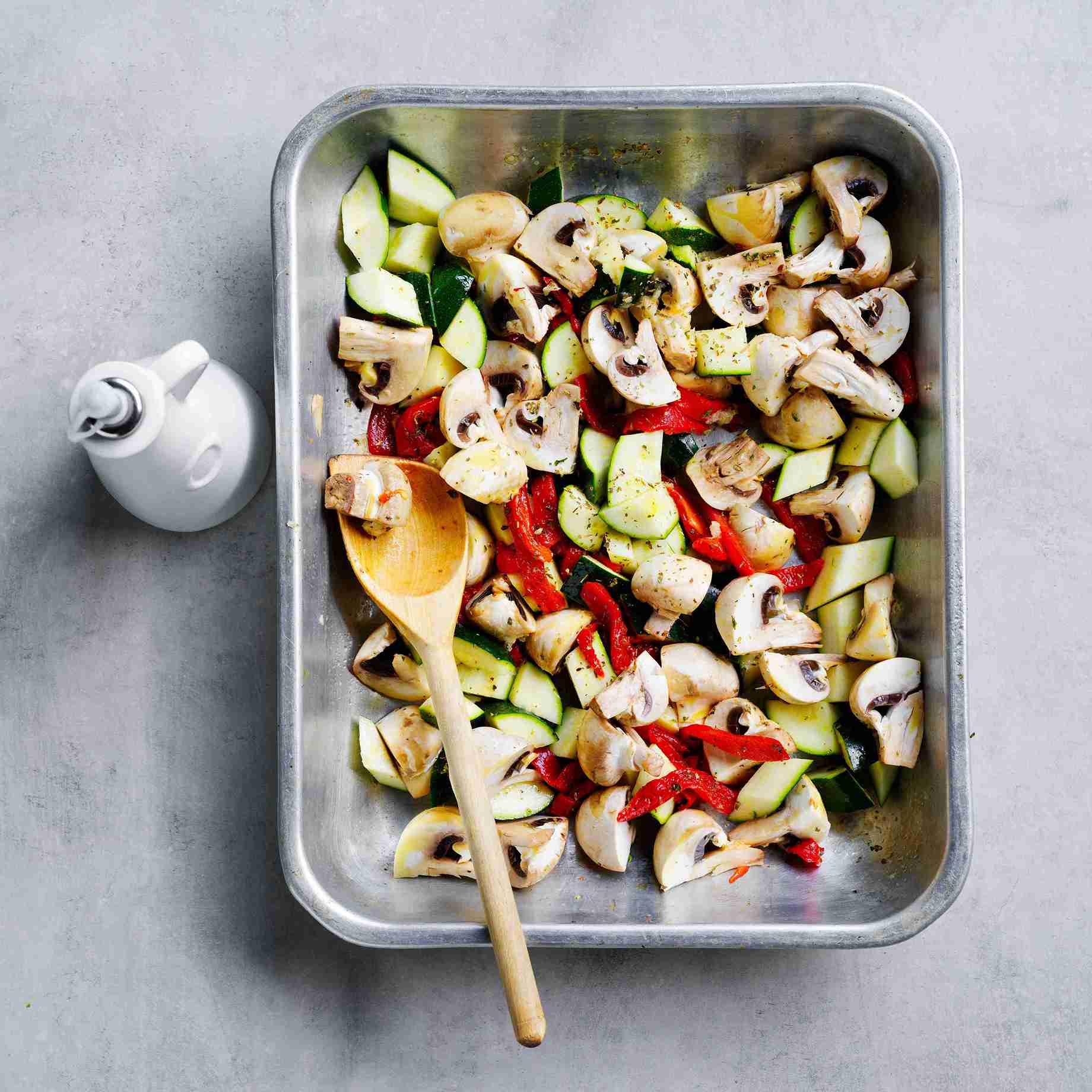 vegetables tossed with herbs and olive oil in a roasting pan, ready for baking