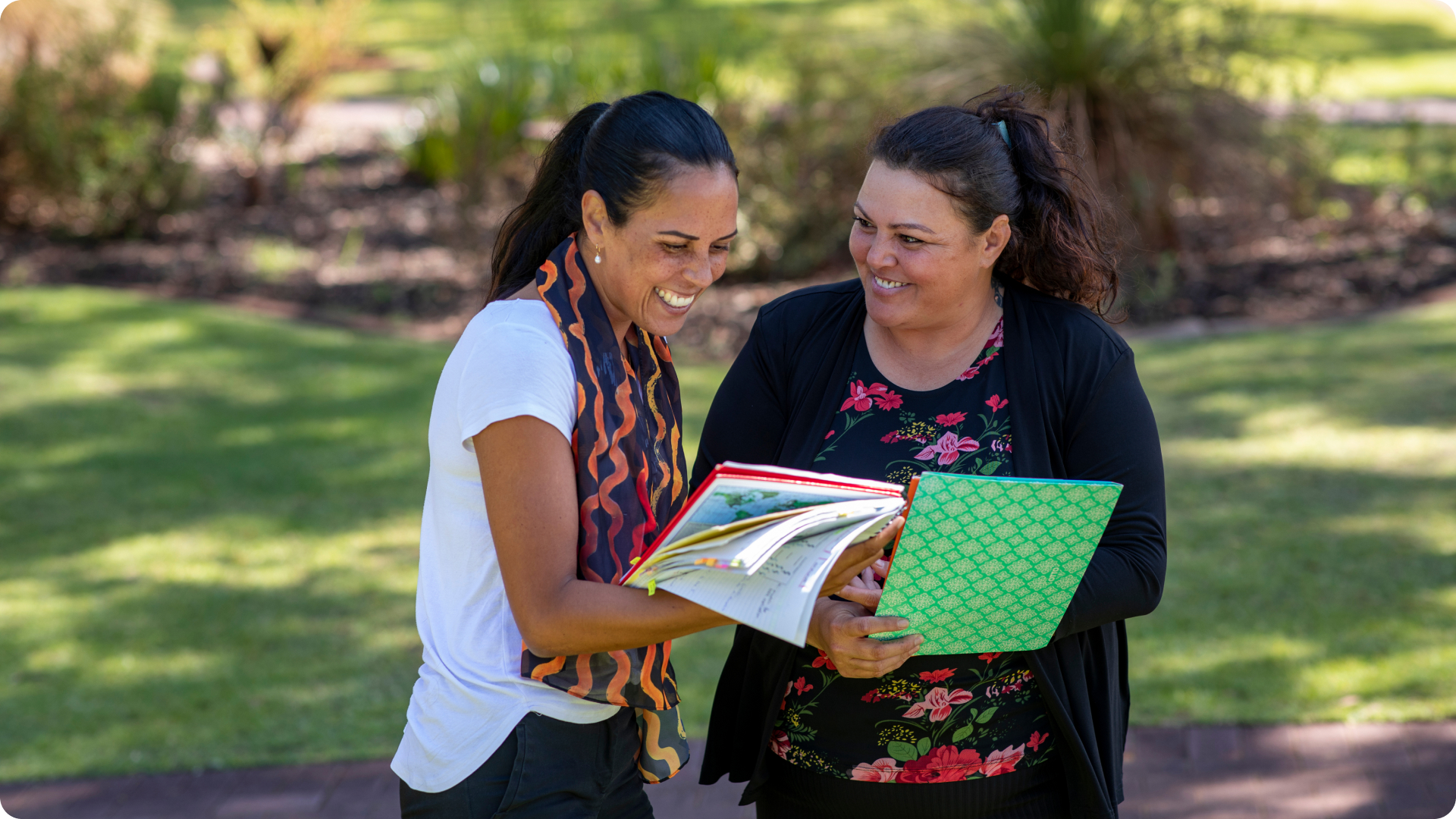 Two first nations women smiling while having a meeting in the park on a sunny day
