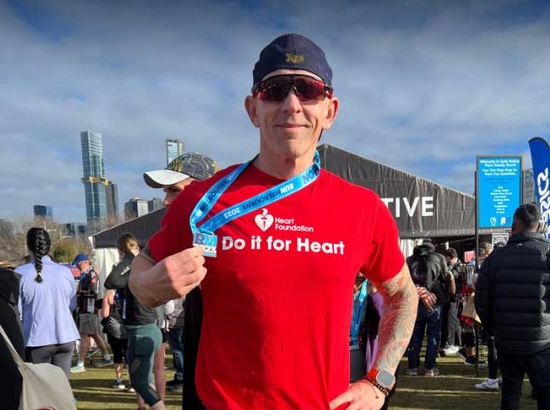 Man in sunglasses, cap and red Do it for Heart t-shirt holding his marathon ribbon smiling