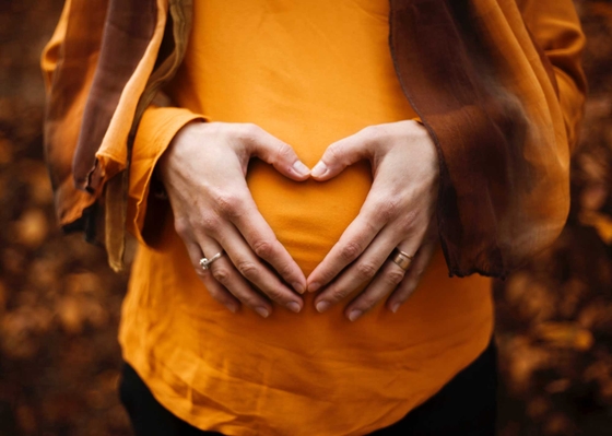 Woman is making a hand heart shape in front of her belly.