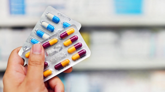 A person holding a pack of pills in front of a pharmacy, symbolizing access to medication and healthcare.