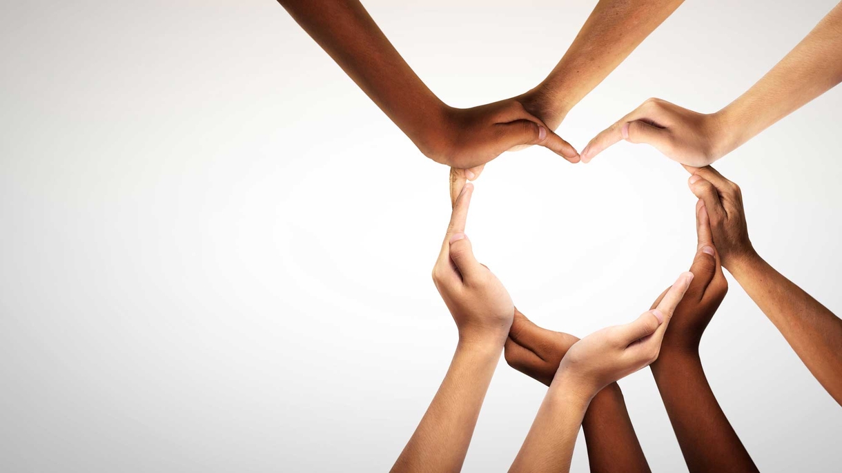 Hands of several people forming a heart shape, with outdoors background