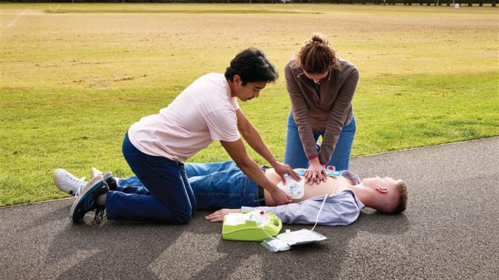A woman and a man doing CPR on a man in cardiac arrest in the park