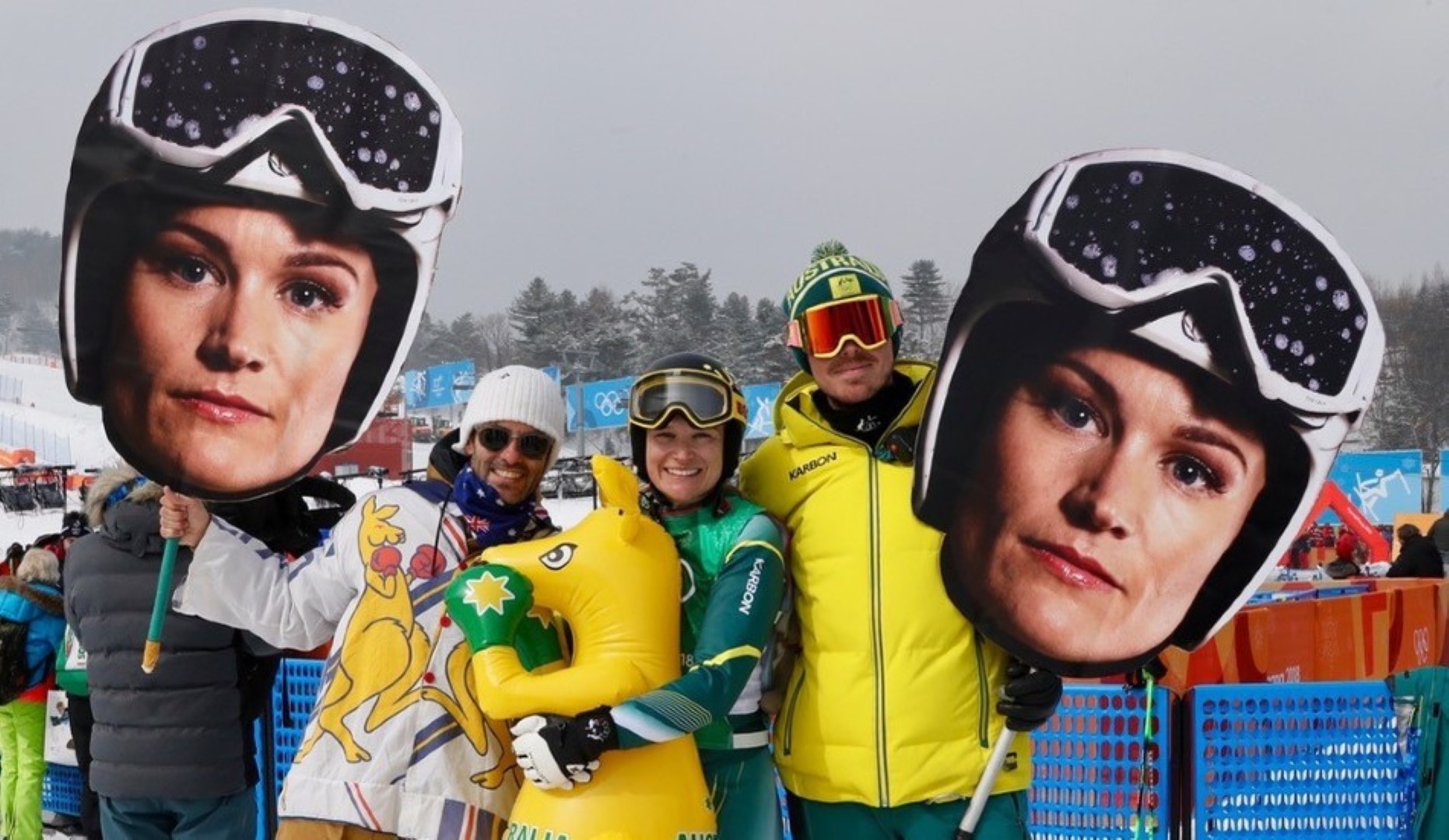 Group of people in the snow holding up signs with Sami Kennedy-Sim's face on them