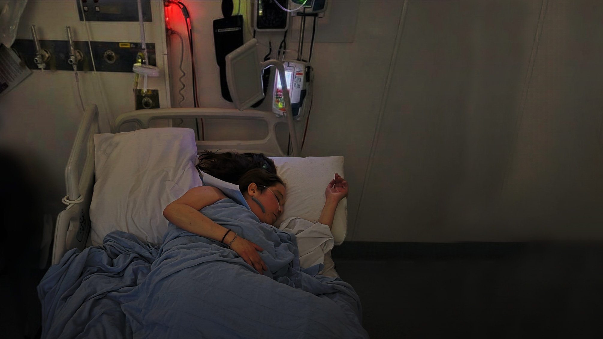 Person resting in a hospital bed with medical monitoring equipment in an Australian hospital room