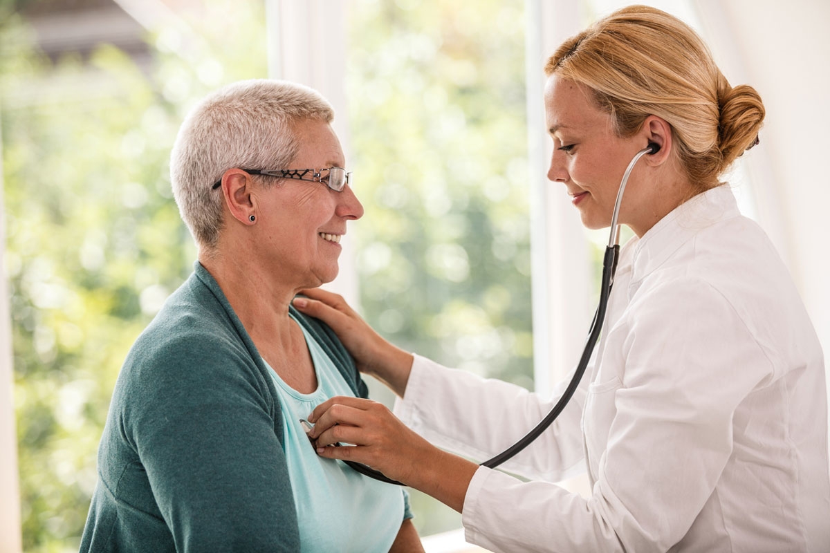 Female GP checking heart of mature woman with short grey hair with stethoscope