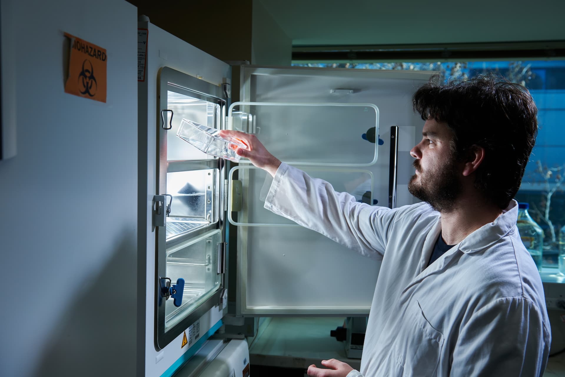 Dr Jarmon Lees in a lab coat places a transparent container inside a cold storage unit 