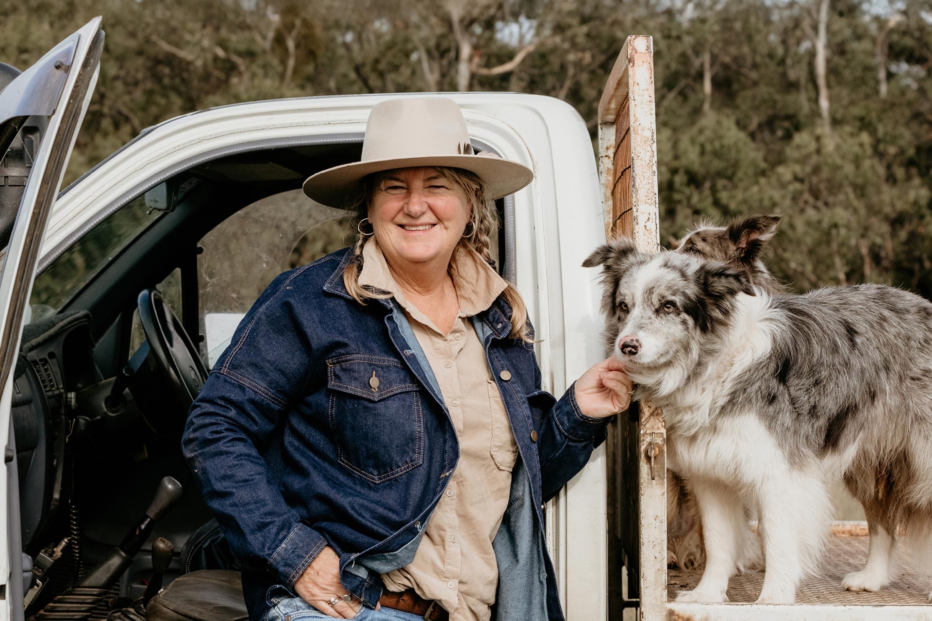 A woman standing next to her ute, and patting her dog