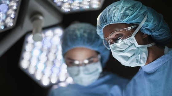Two surgeons in blue scrubs and masks focus intently under bright surgical lights for a bypass surgery.