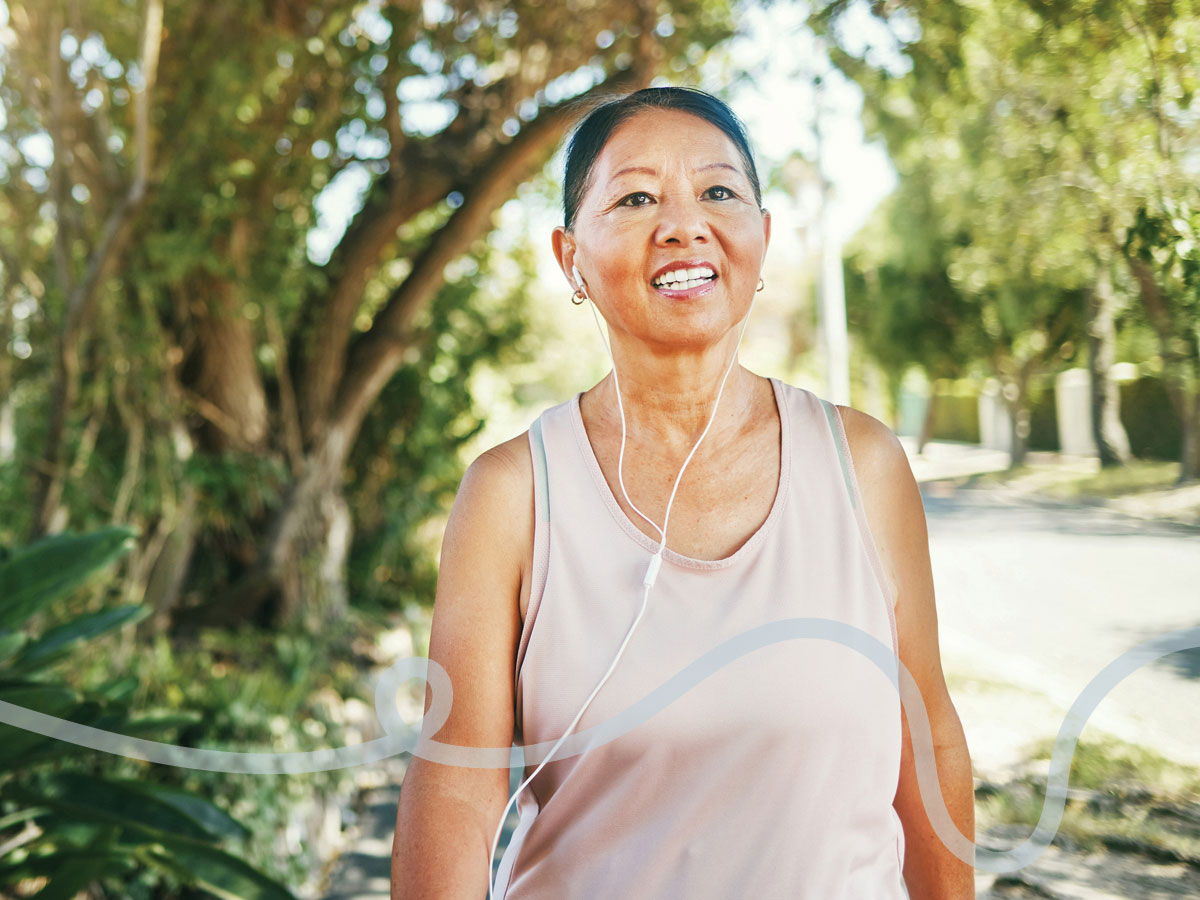 Smiling woman listening with mobile earplugs, walking through a park