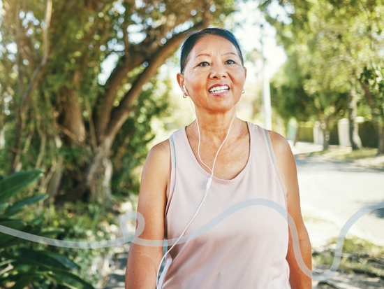 Smiling woman listening with mobile earplugs, walking through a park