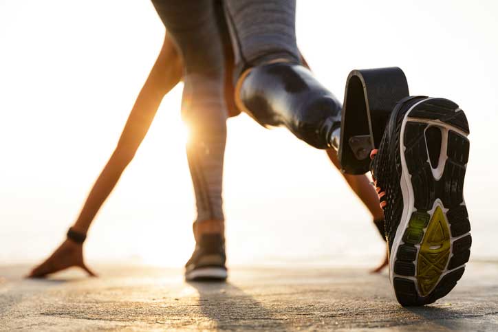 Athlete with a running blade prosthetic leg in a starting position on a sunny outdoor track
