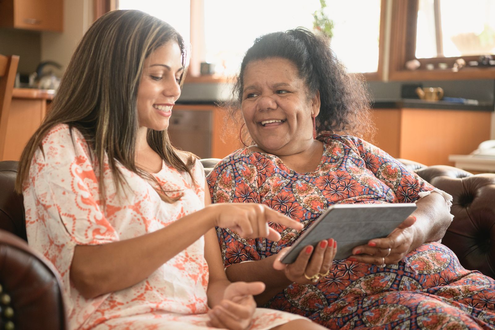 A woman and her mother engrossed in a tablet while sitting on a couch.