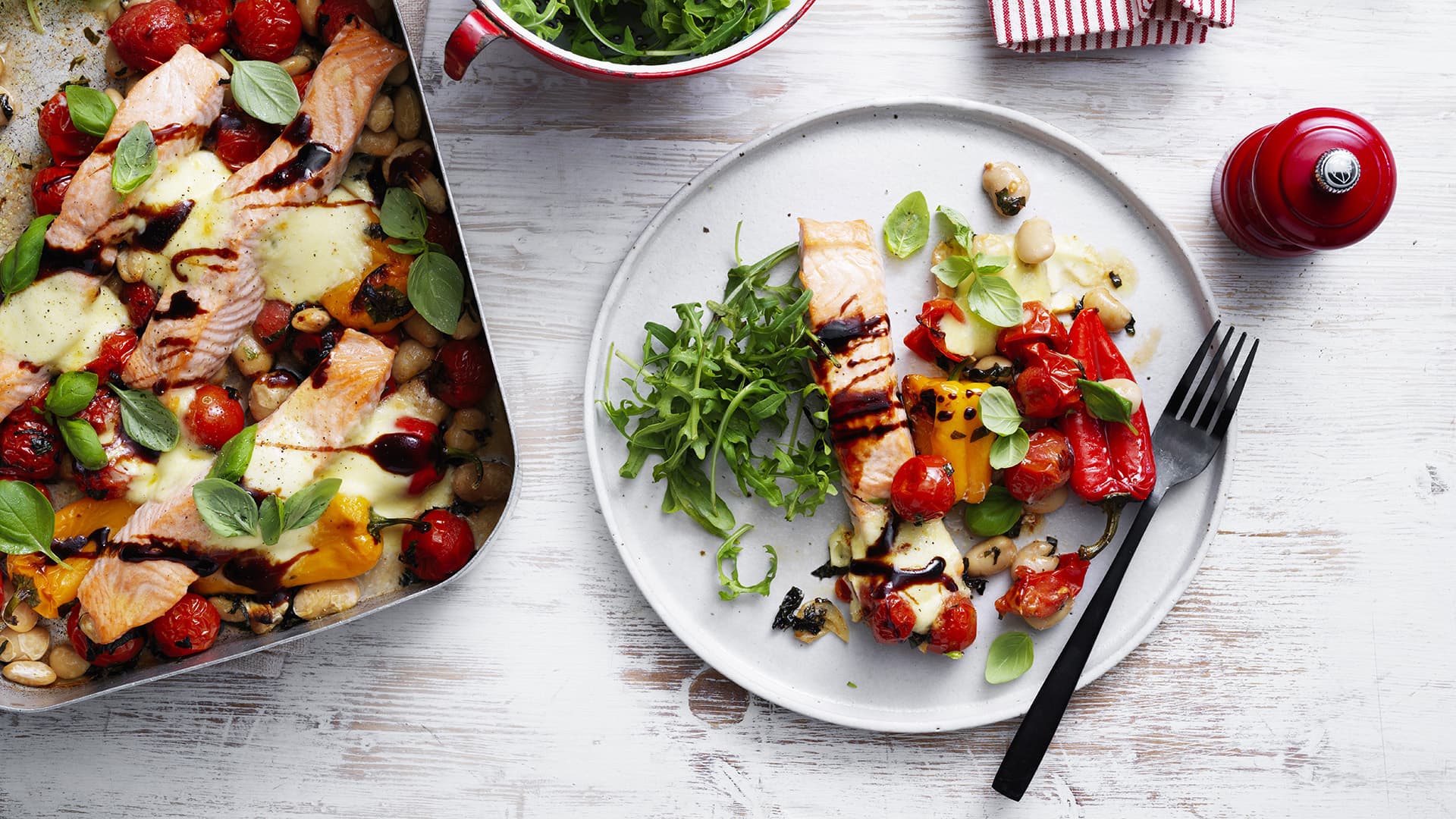 A baking dish and a plate, each containing the One pan salmon caprese bake, is arranged on a table