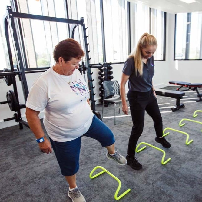 Two people stepping over agility hurdles during a supervised exercise session in a gym
