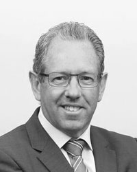 Mike McKenna wearing glasses and a suit in a black and white photo.