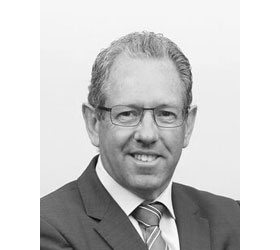 Mike McKenna wearing glasses and a suit in a black and white photo.