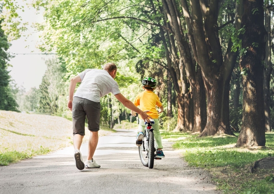 A man helping his child joyfully ride a bike along a scenic path, enjoying a moment of togetherness and adventure.