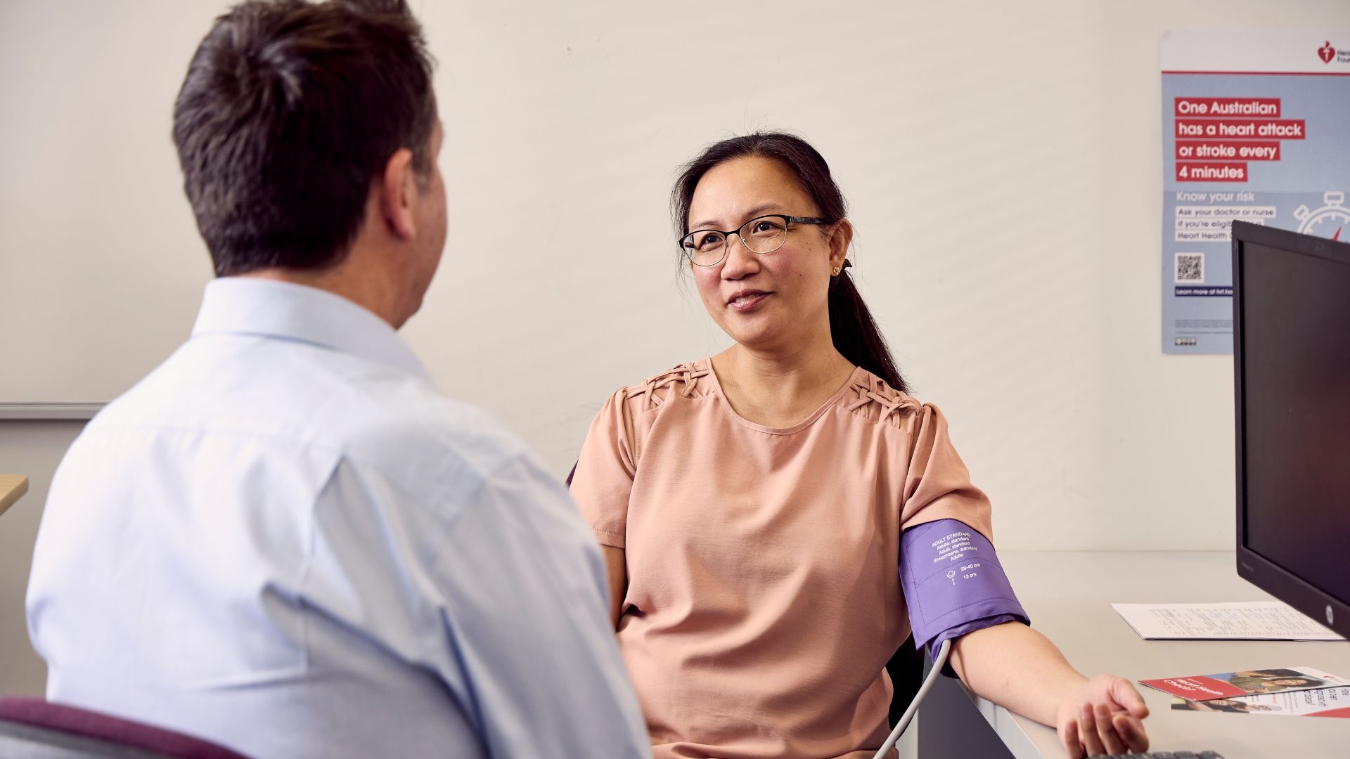A doctor running a blood pressure check on a patient sitting on a GP desk