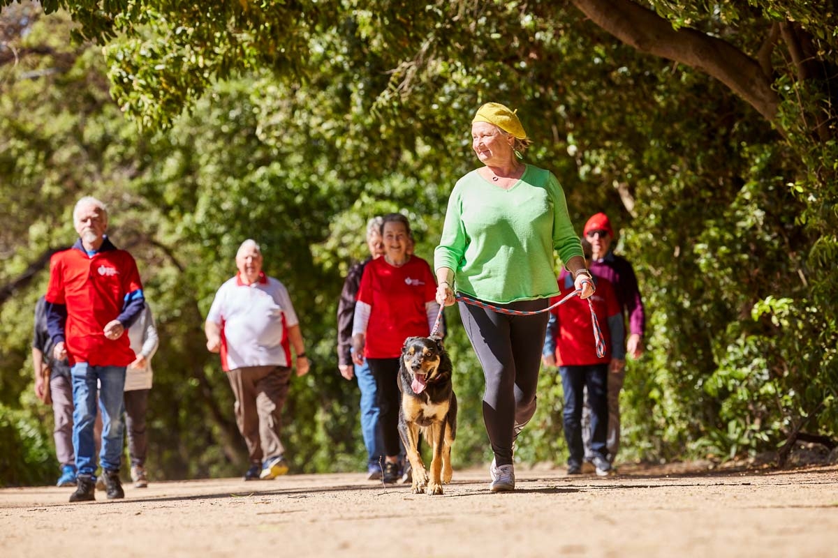 Group of people walking outdoors, a woman in a green jumper is ahead with her dog