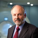 David Hare in business attire stands before an MRI machine.
