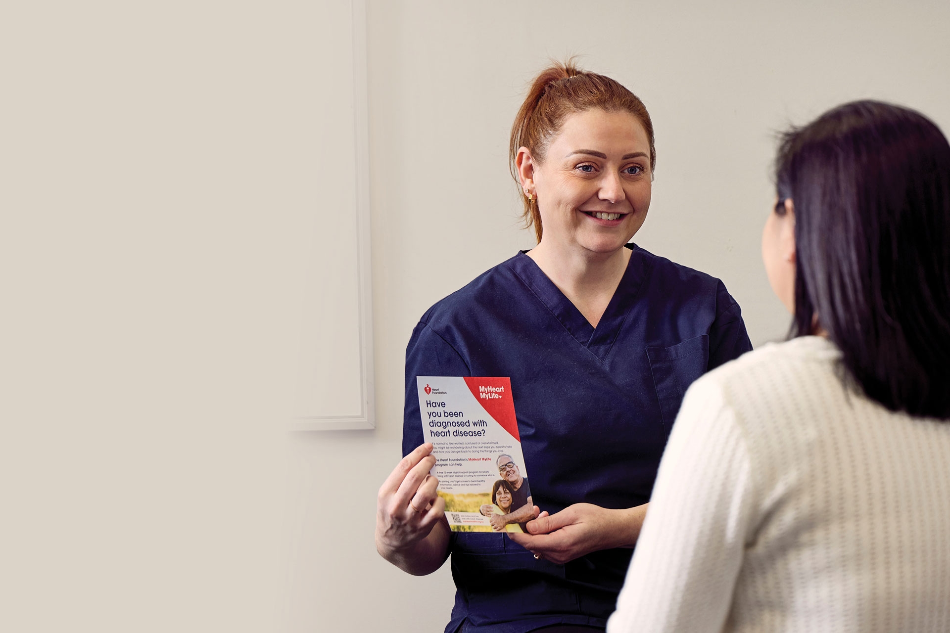 A nurse holding a MyHeart MyLife flyer, and showing it to a patient