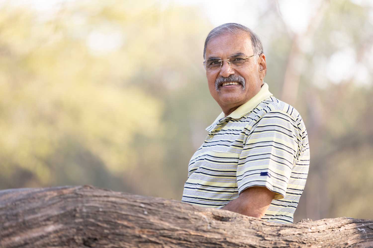 Smiling man with a moustache, striped polo shirt, and glasses, outdoors
