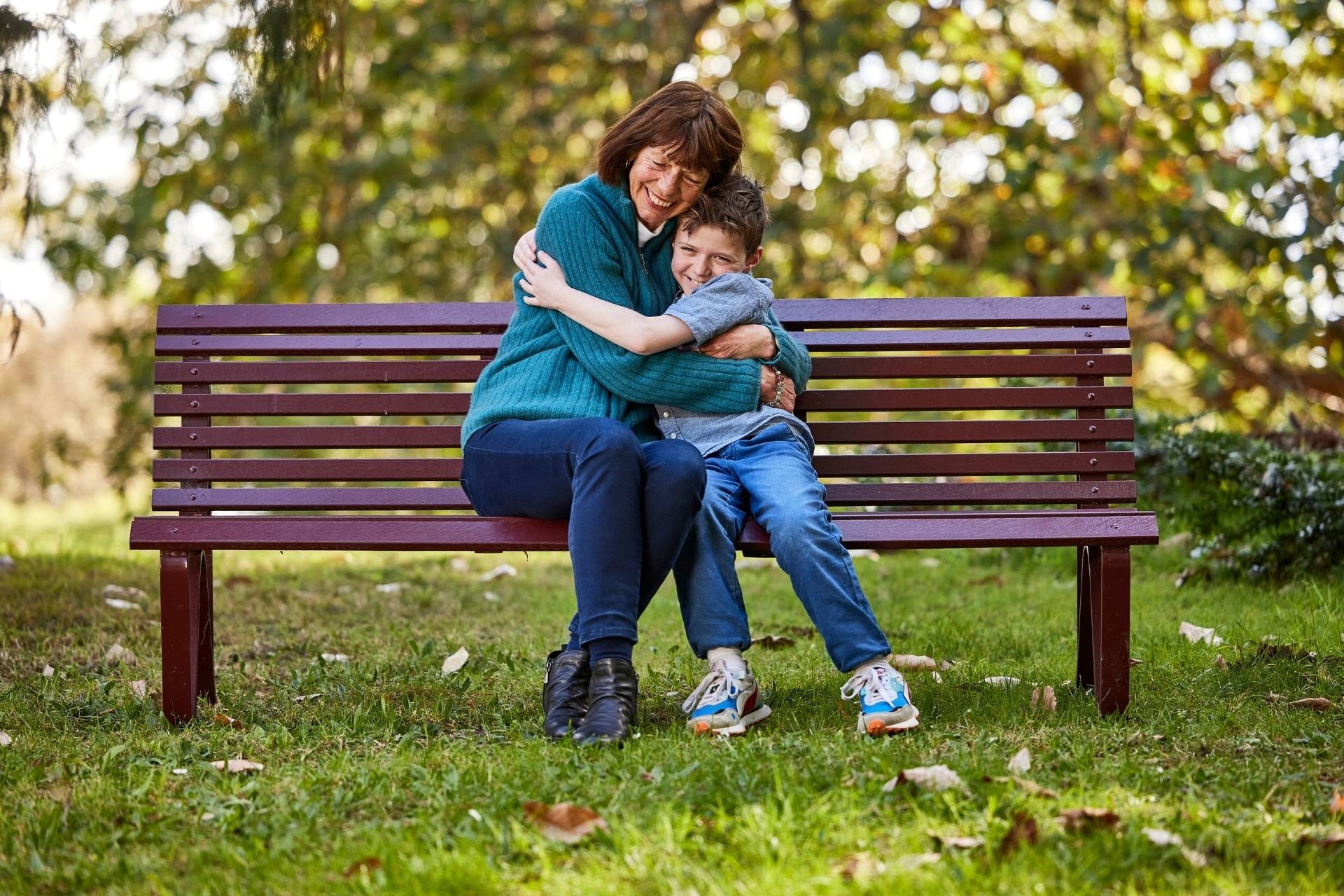 An older woman and her grandson hugging on a bench in a leafy park