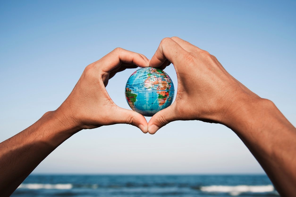 World map in heart-shaped hands on a beach, symbolizing love for global unity and exploration.
