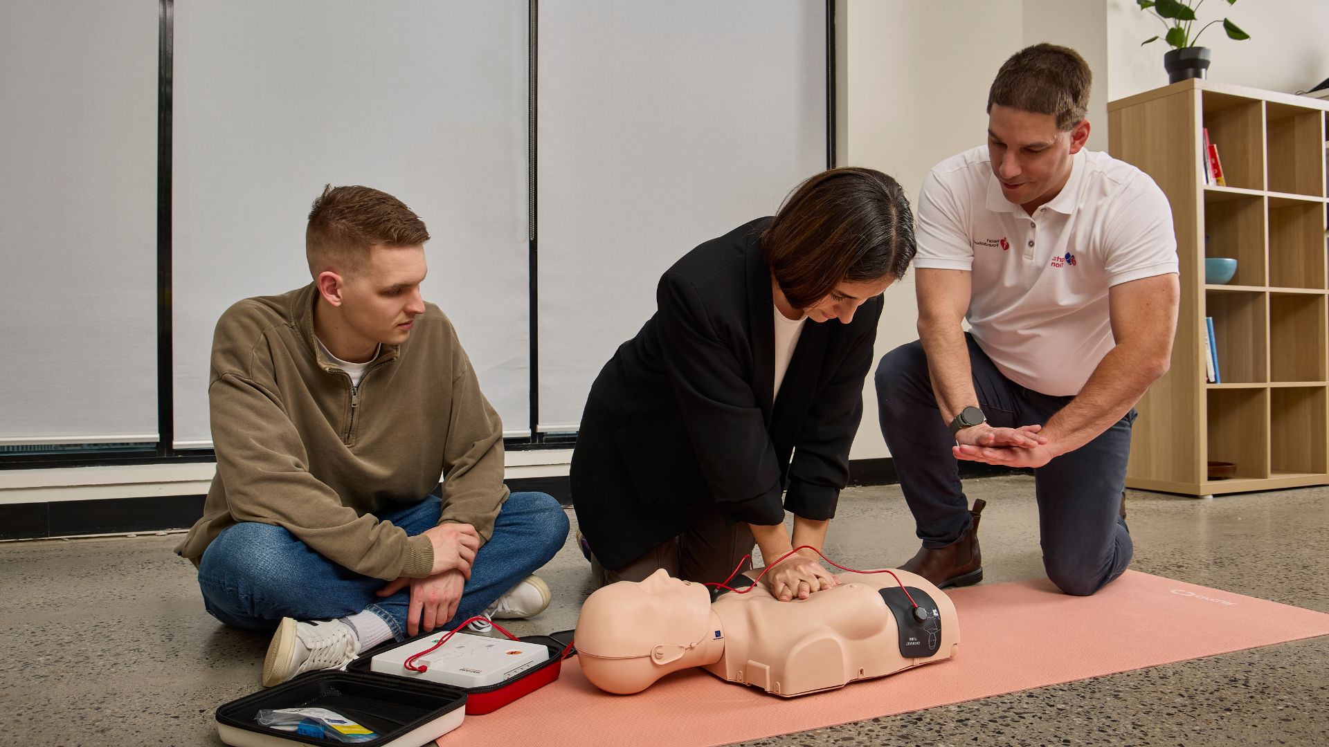 A couple of people learning how to do compressions on a mannequin