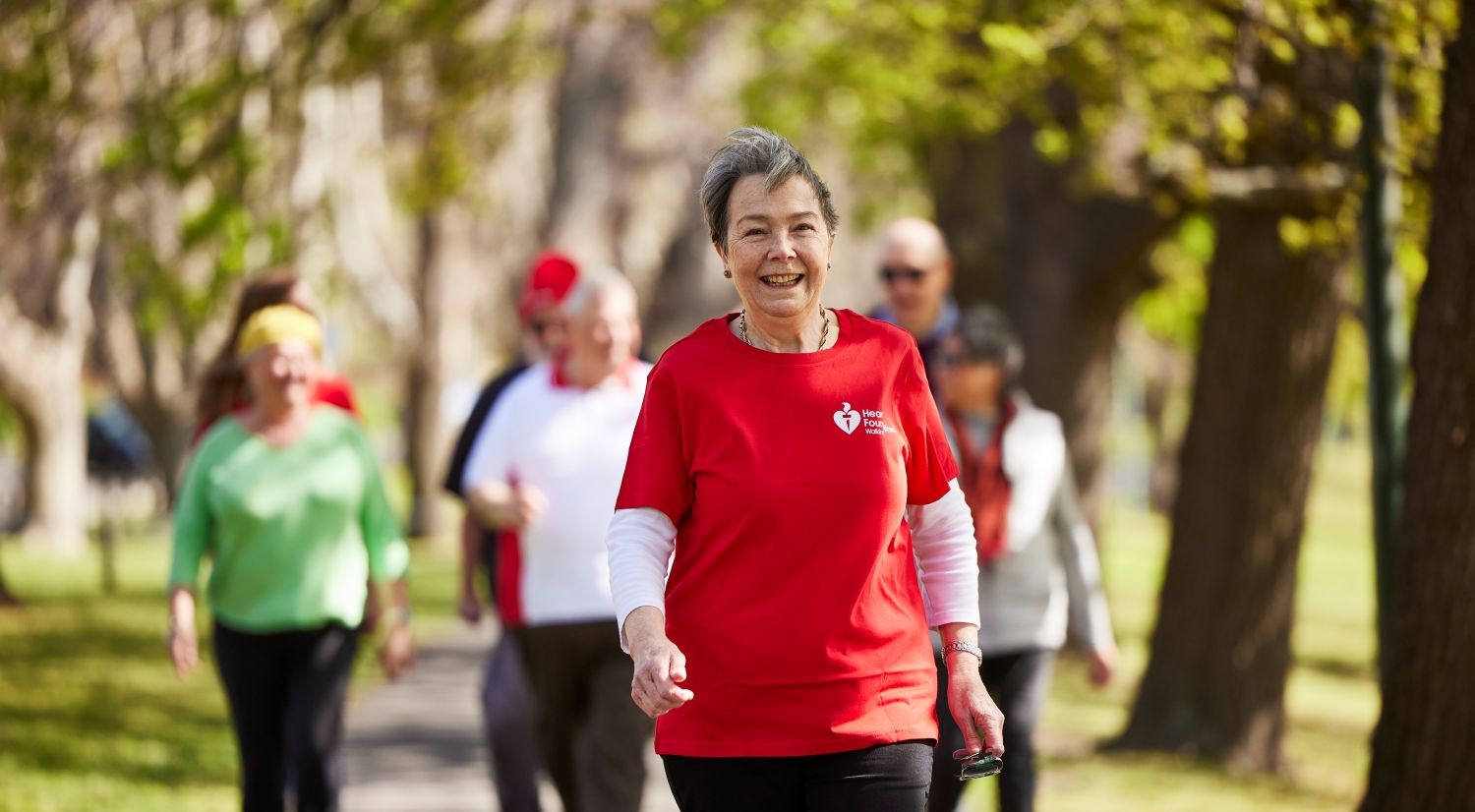 People walking together along a tree‑lined path as part of a community exercise activity.