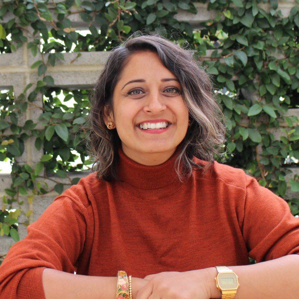 Jaina Chauhan in an orange sweater enjoying a peaceful moment on a bench.