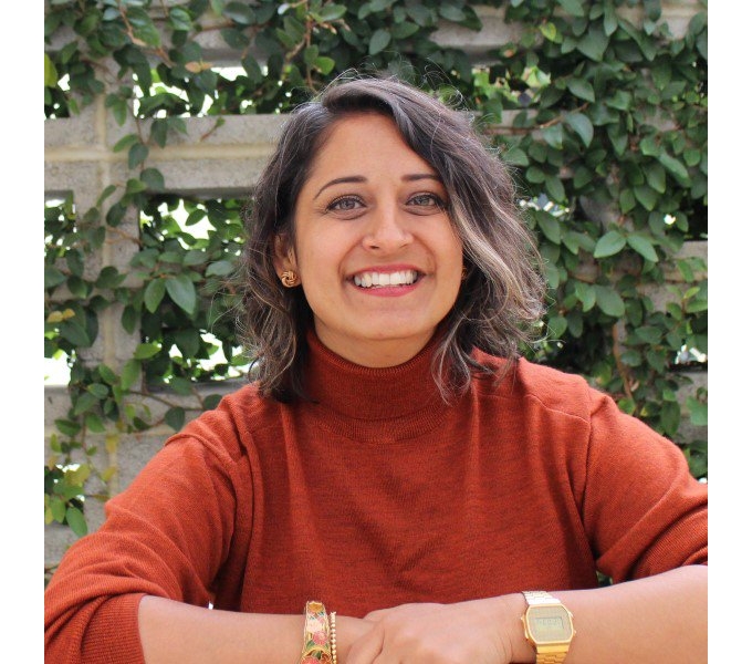 Jaina Chauhan in an orange sweater enjoying a peaceful moment on a bench.