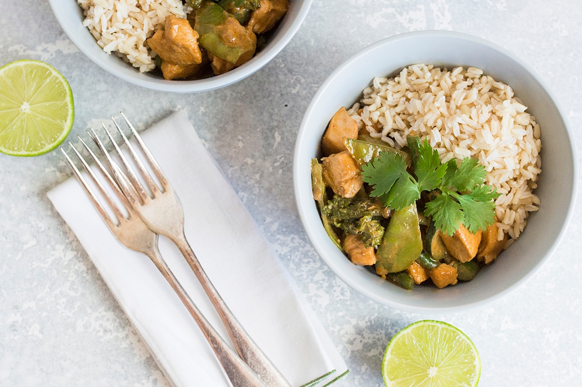 two bowls of rice, chicken and vegetables, and lime wedges on top