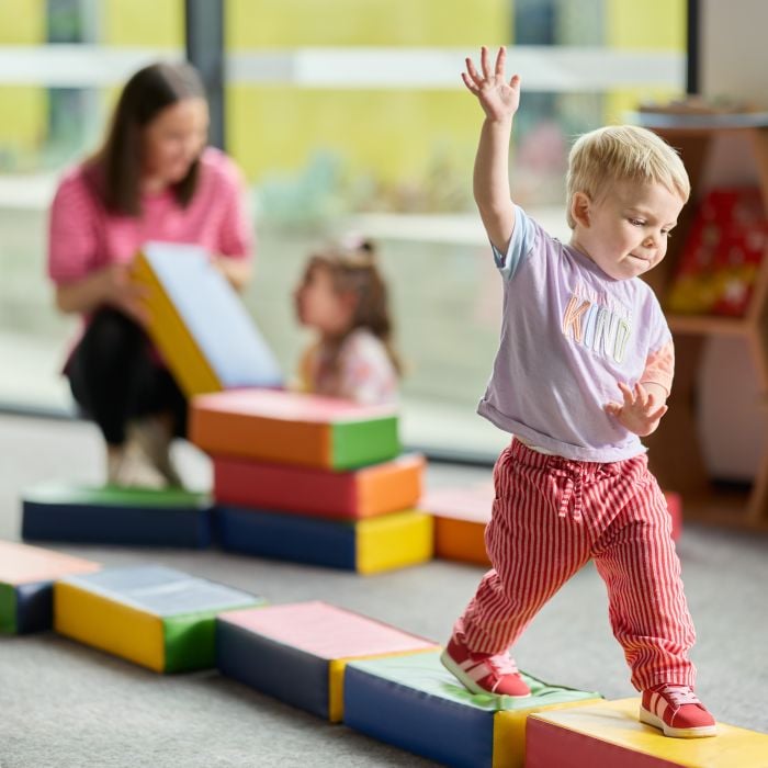 Child balancing on colourful play blocks indoors during an early learning activity
