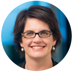 A woman with glasses and a black jacket smiling, radiating warmth and confidence.