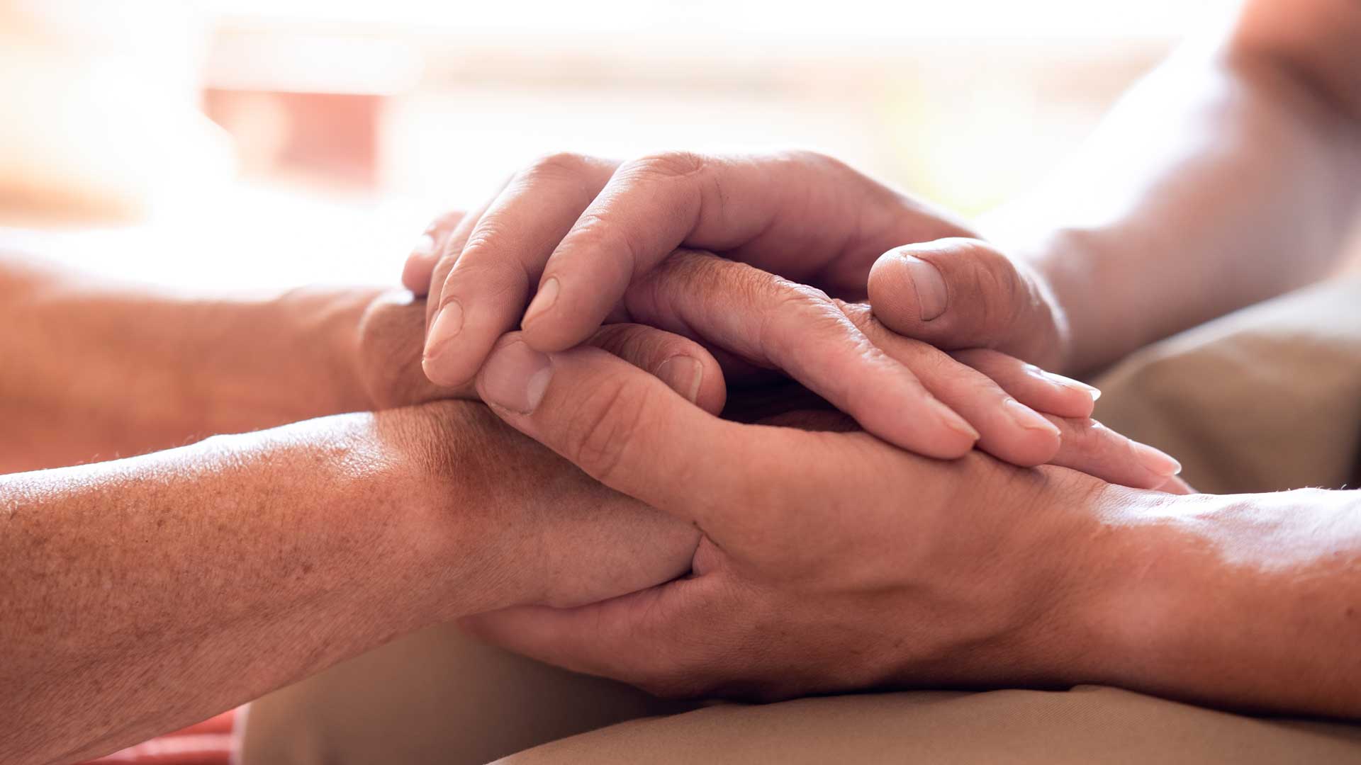 A man's hand stroking the hands of another in support