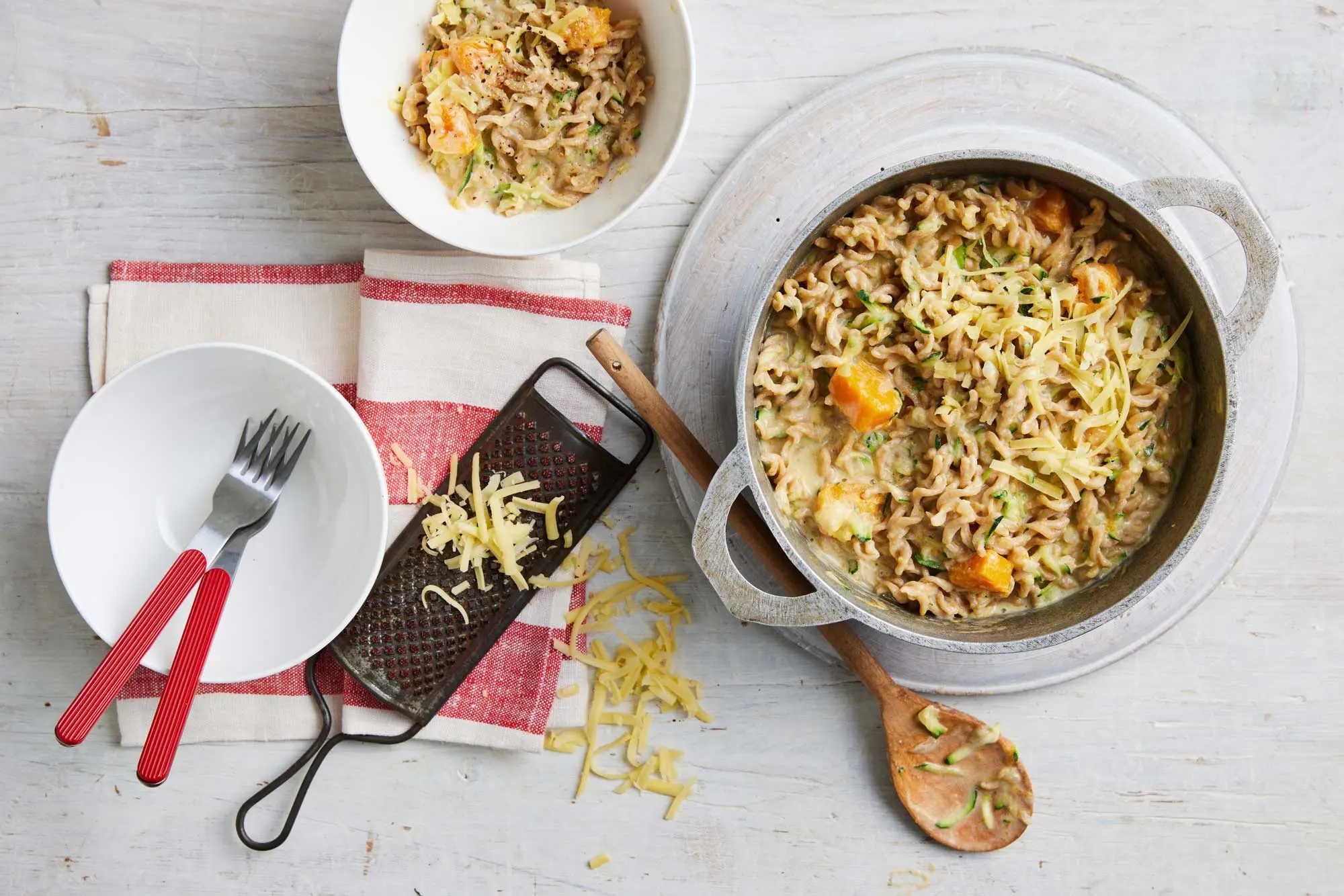 A colourful bowl of pasta with cheese and fresh vegetables.