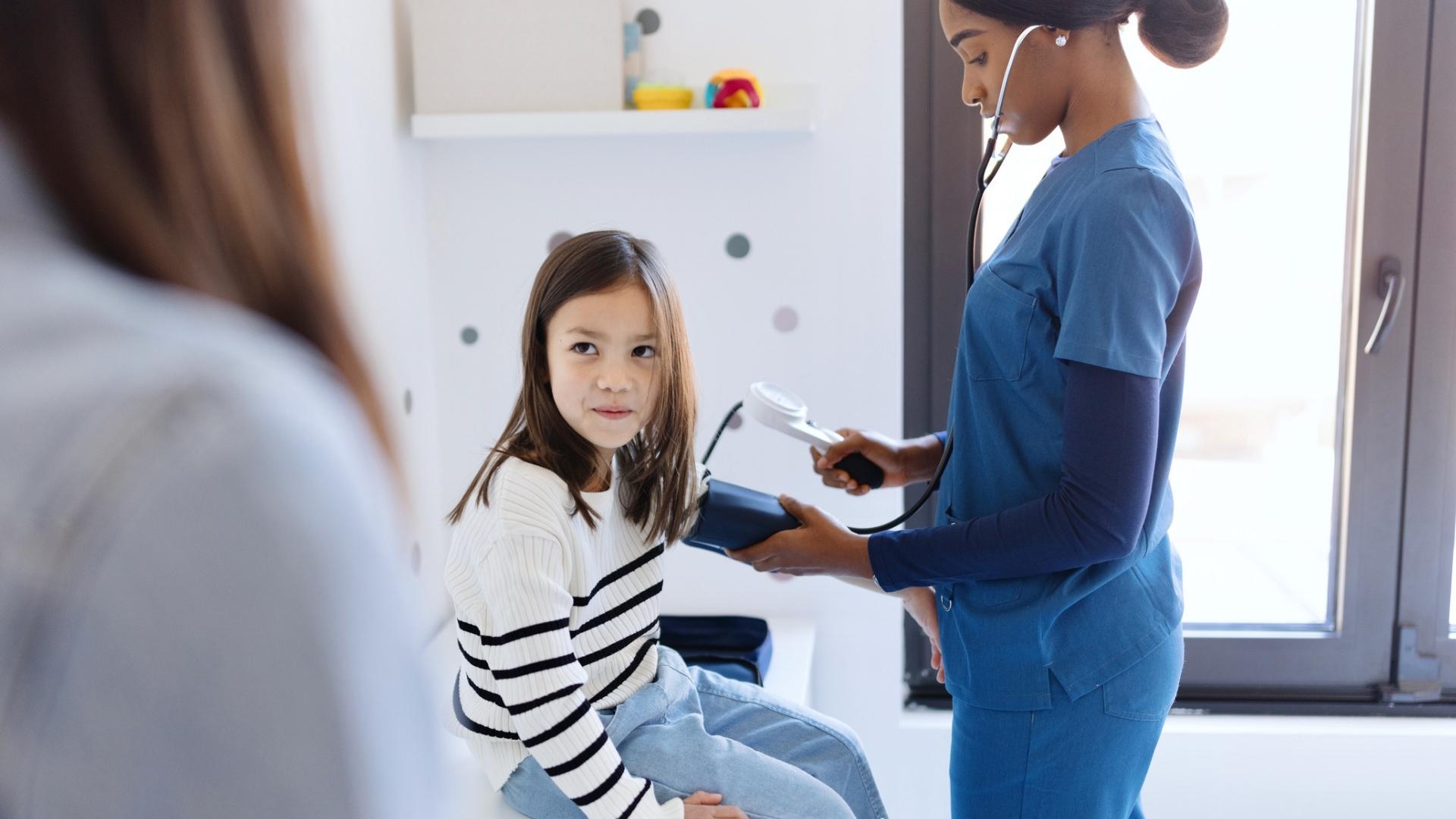Nurse checking young girl's blood pressure while child looks at mum